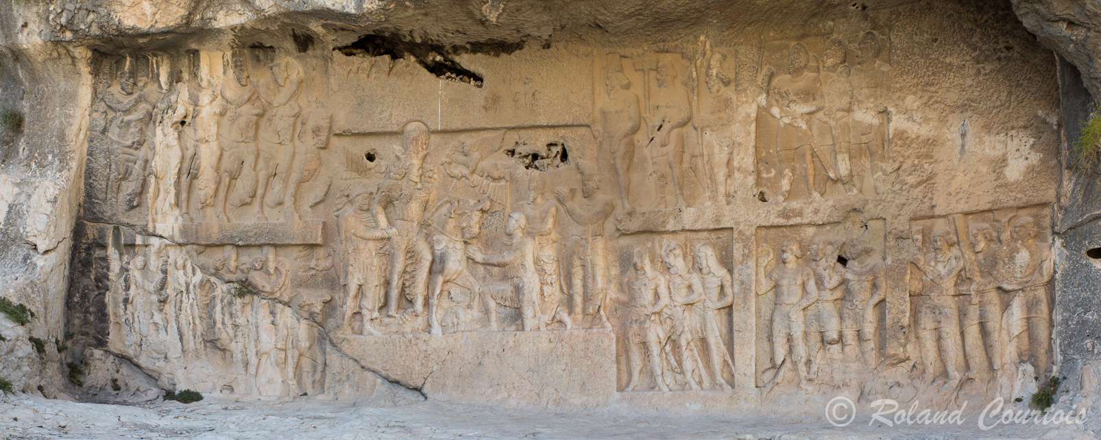 Sur les rives du Band-i Shapur, Ce bas-reliefs commémore les victoires de Shâpur Ier sur les Romains. Le roi reçoit le diadème  et cette scène triomphale est entourée à droite de porteurs d’offrandes (en 5 cadres séparés) et à gauche de la cavalerie perse sur deux rangées.