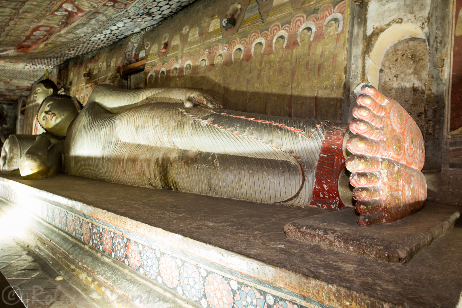 Grottes de Dambulla. Grand Bouddha couché avec le drapé rayé et le coussin. Et derrière les moines qui veillent le Bouddha.